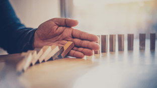 A hand stopping a line of dominos from falling down