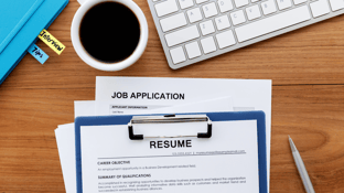 Resume on a clip board, next to a job application, a computer keyboard and a coffee cup