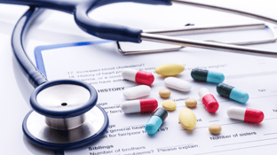 Stethoscope with patient chart covered with assorted, multi-colored capsuled pills