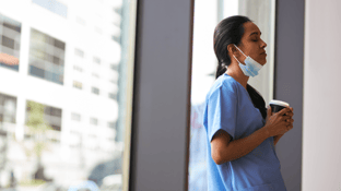 Clinical employee leaning against a window, holding a coffee cup, eyes closed and taking a break.