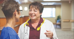 Woman in lab coat talking to woman in scrubs TreeTree_Heartland-3795-1