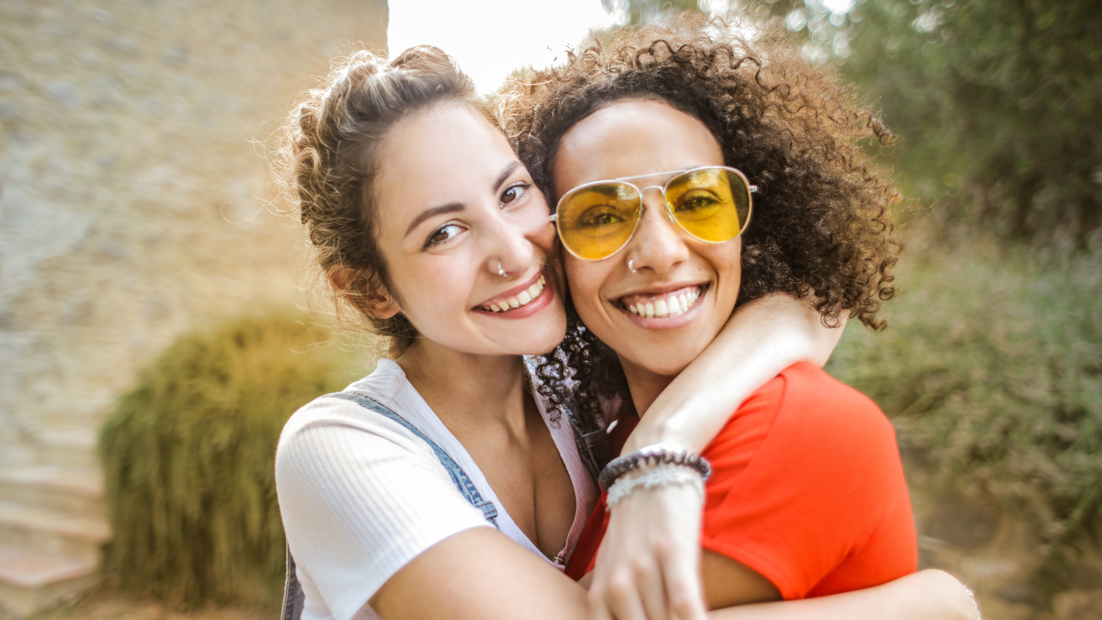 Two young ladies hugging and smiling outside