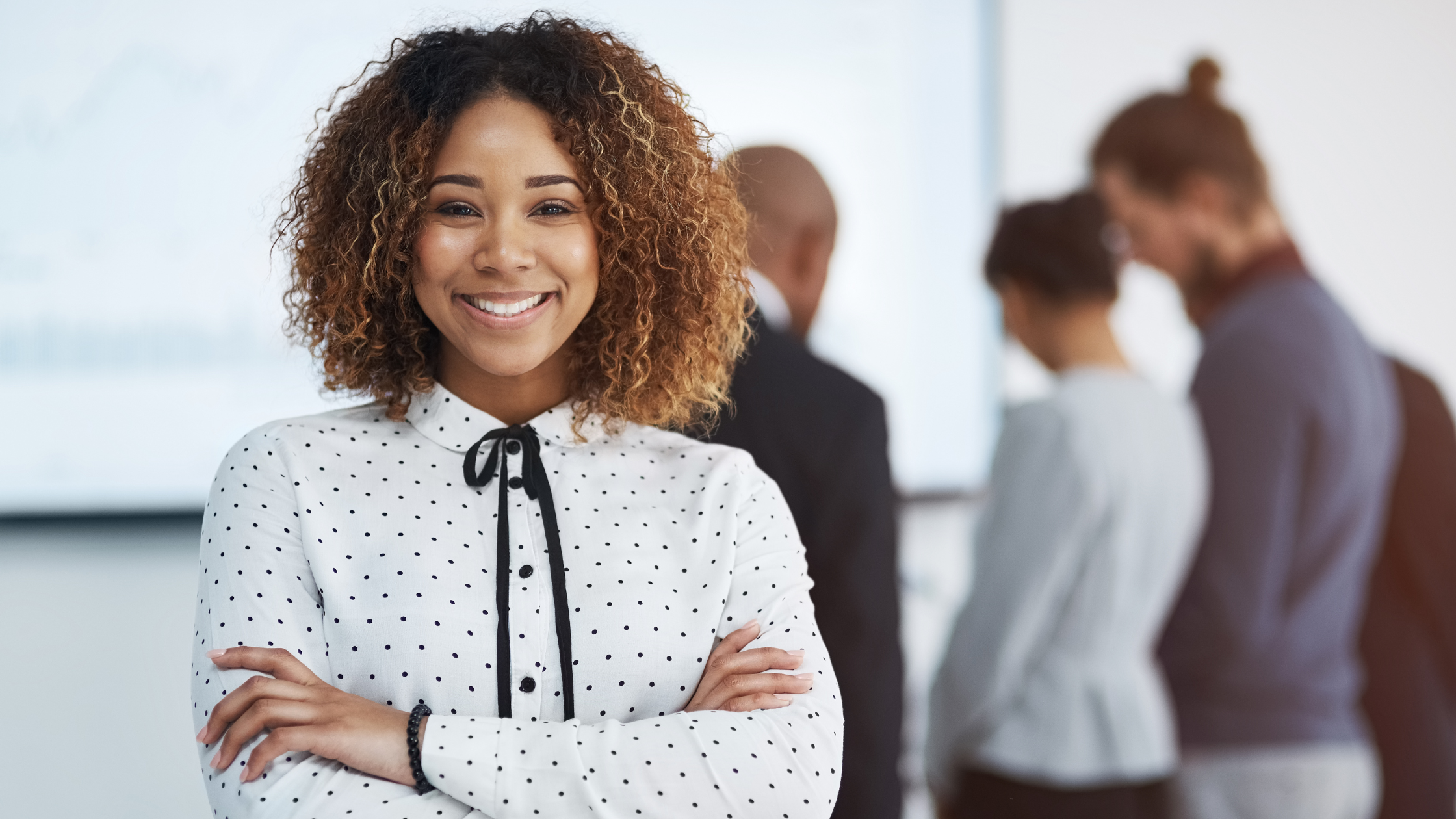 Smiling woman standing with arms crossed in front of group of people